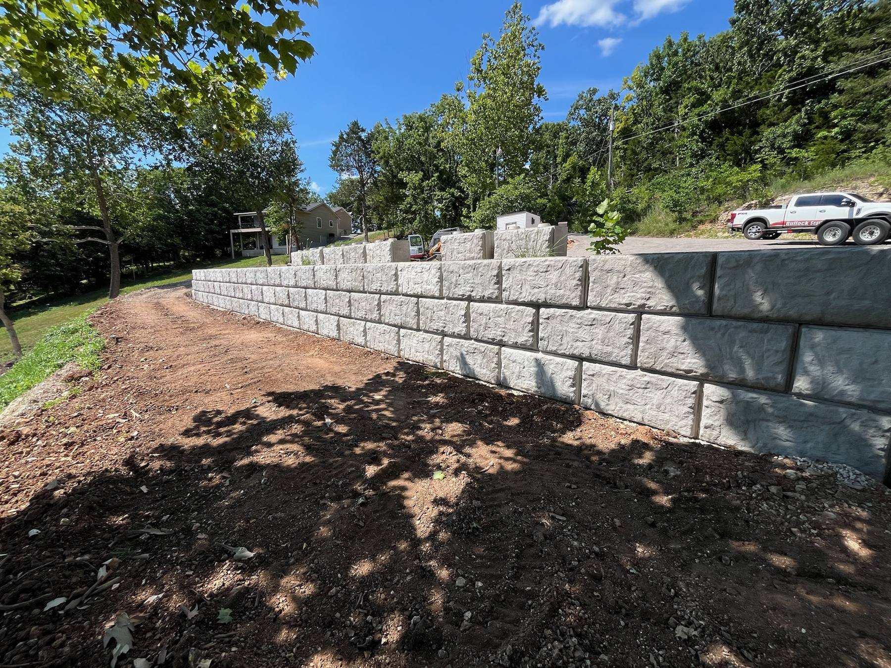 A long big-block retaining wall running along a freshly graded drive on a sunny day