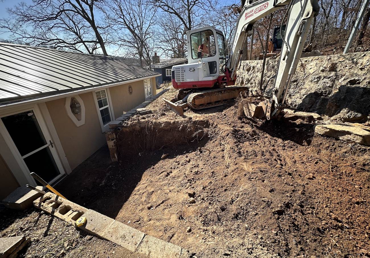 Excavator digging along the side of a house for foundation and drainage work