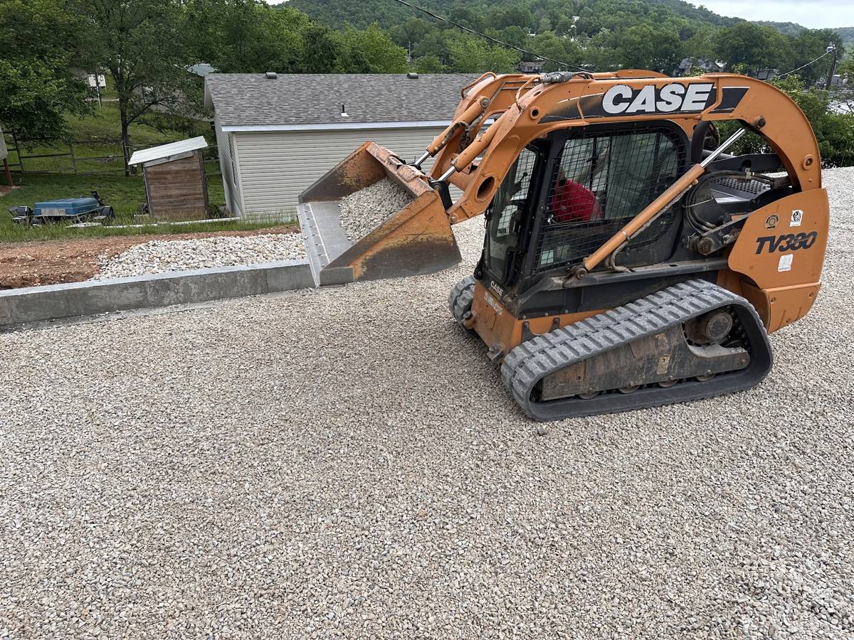 Track loader carrying a bucket of gravel beside a poured curb