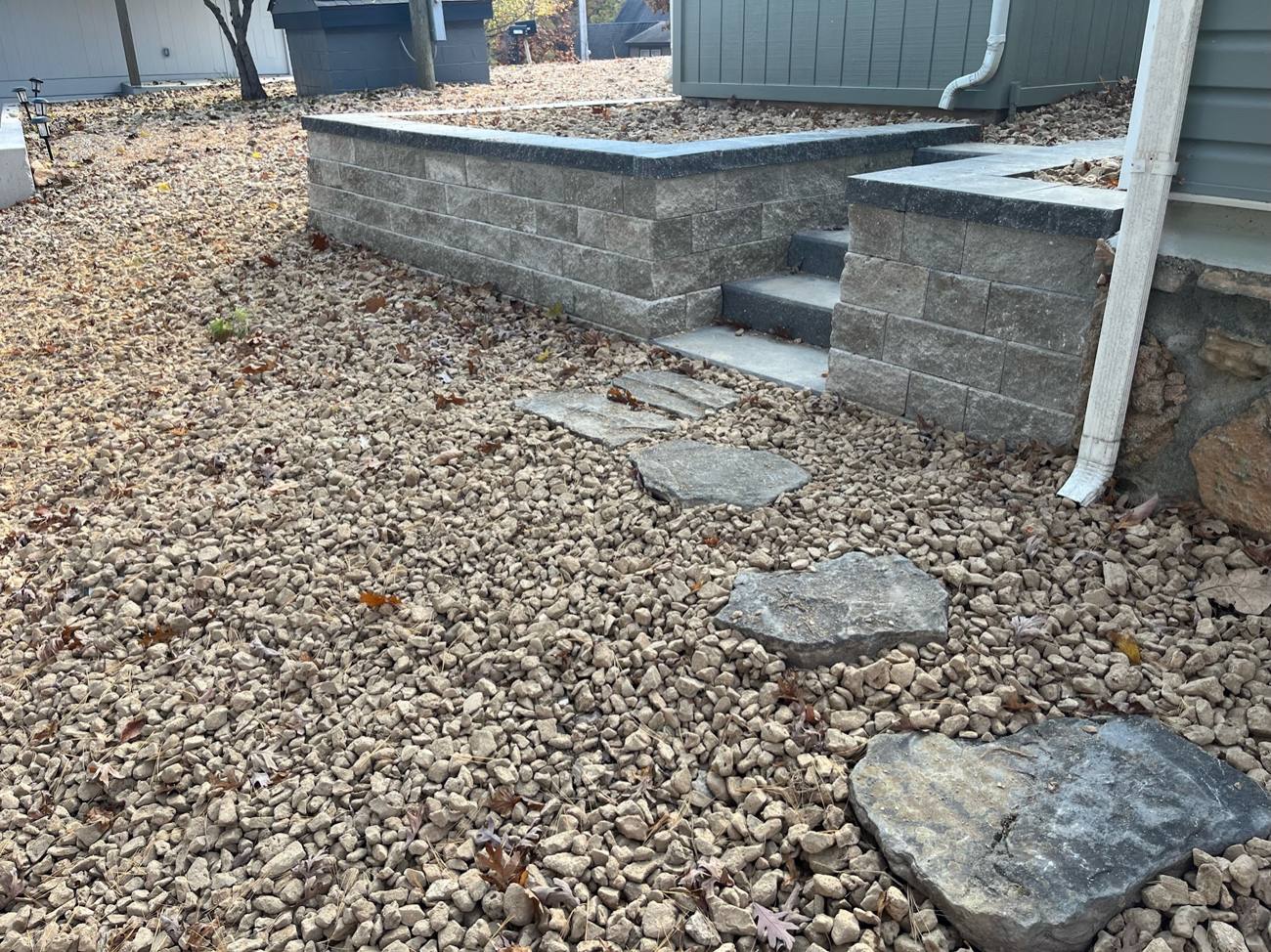 Finished retaining wall with steps and rock landscaping beside a house